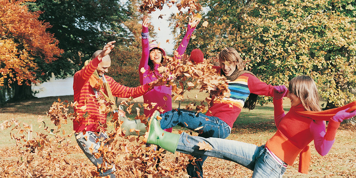 Group of Young Men and Women Kicking Leaves in a Park